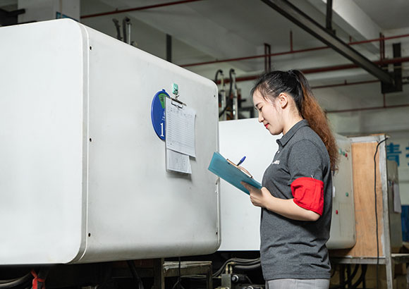 a female worker is checking machine operation and standing beside an injection machine